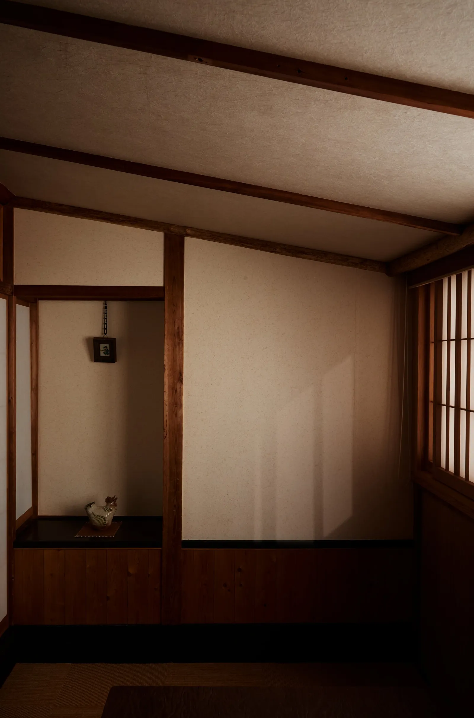 a quiet traditional room with exposed wooden beams, paper screens and a small alcove, lit by soft low light from the right