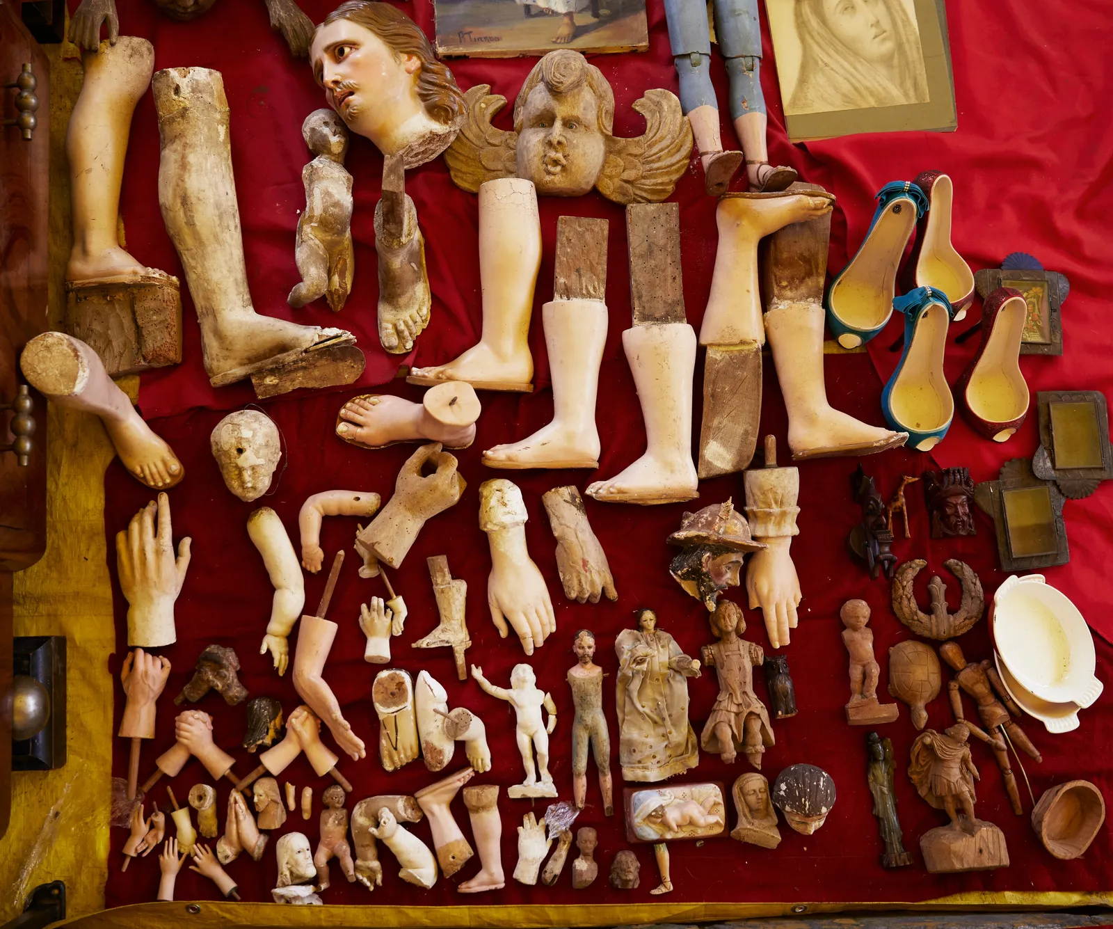 a red cloth covered with old carved wooden limbs, heads, hands and small figures laid out on it