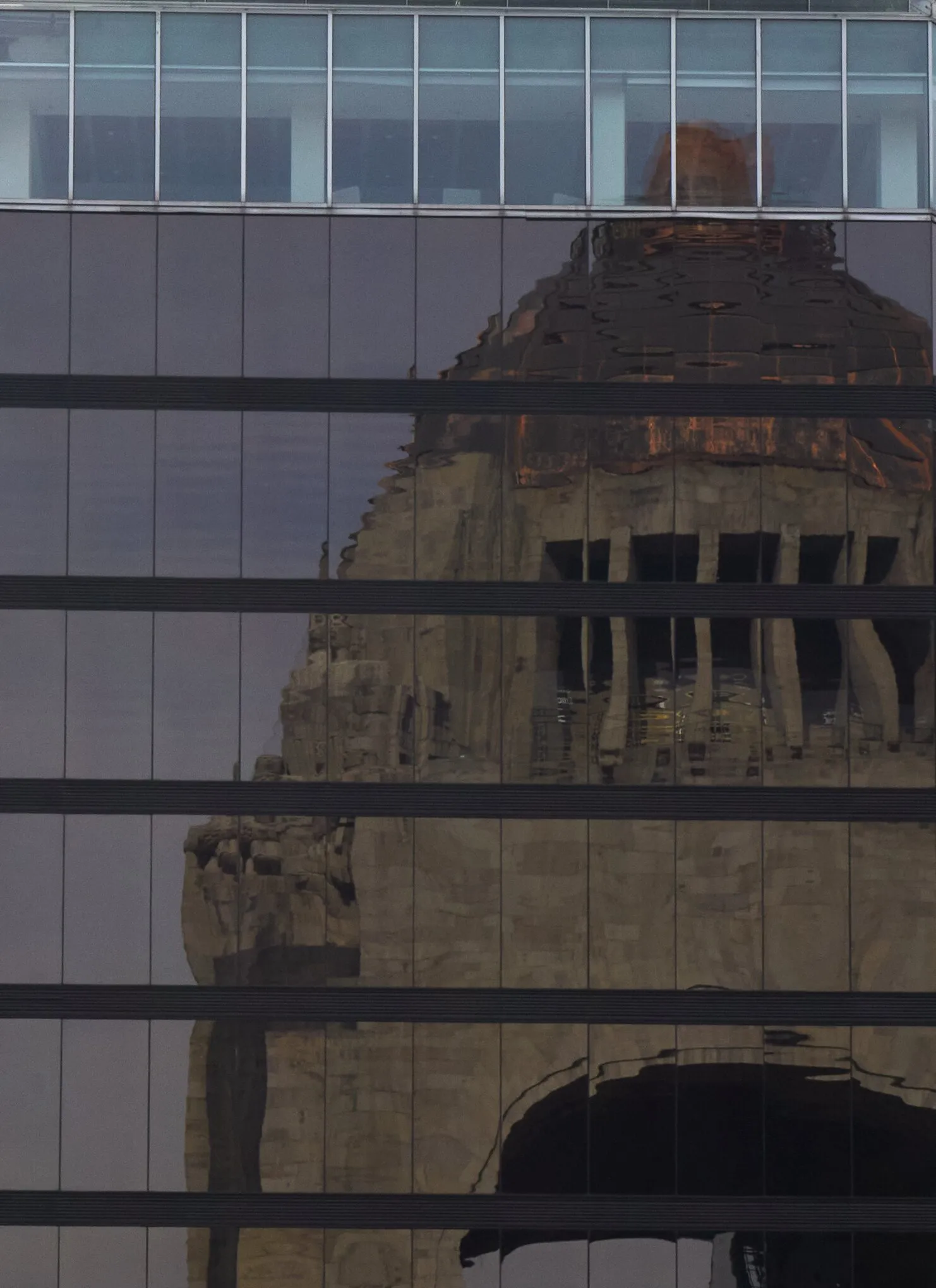 tall glass building facade with dark horizontal bands reflecting a weathered stone monument with a domed top