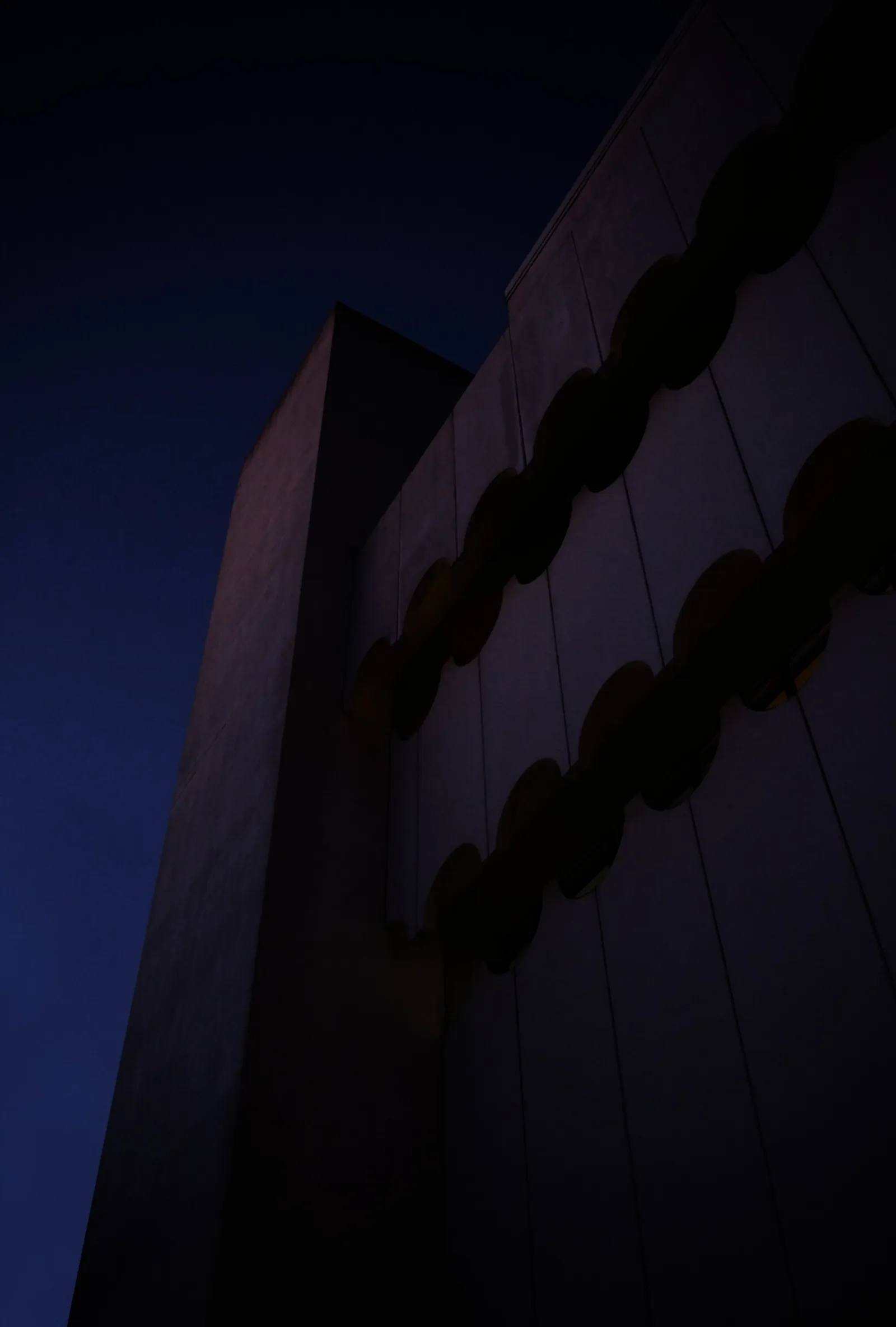 dark building at dusk, its wall banded with scalloped curved forms rising against a deep navy sky