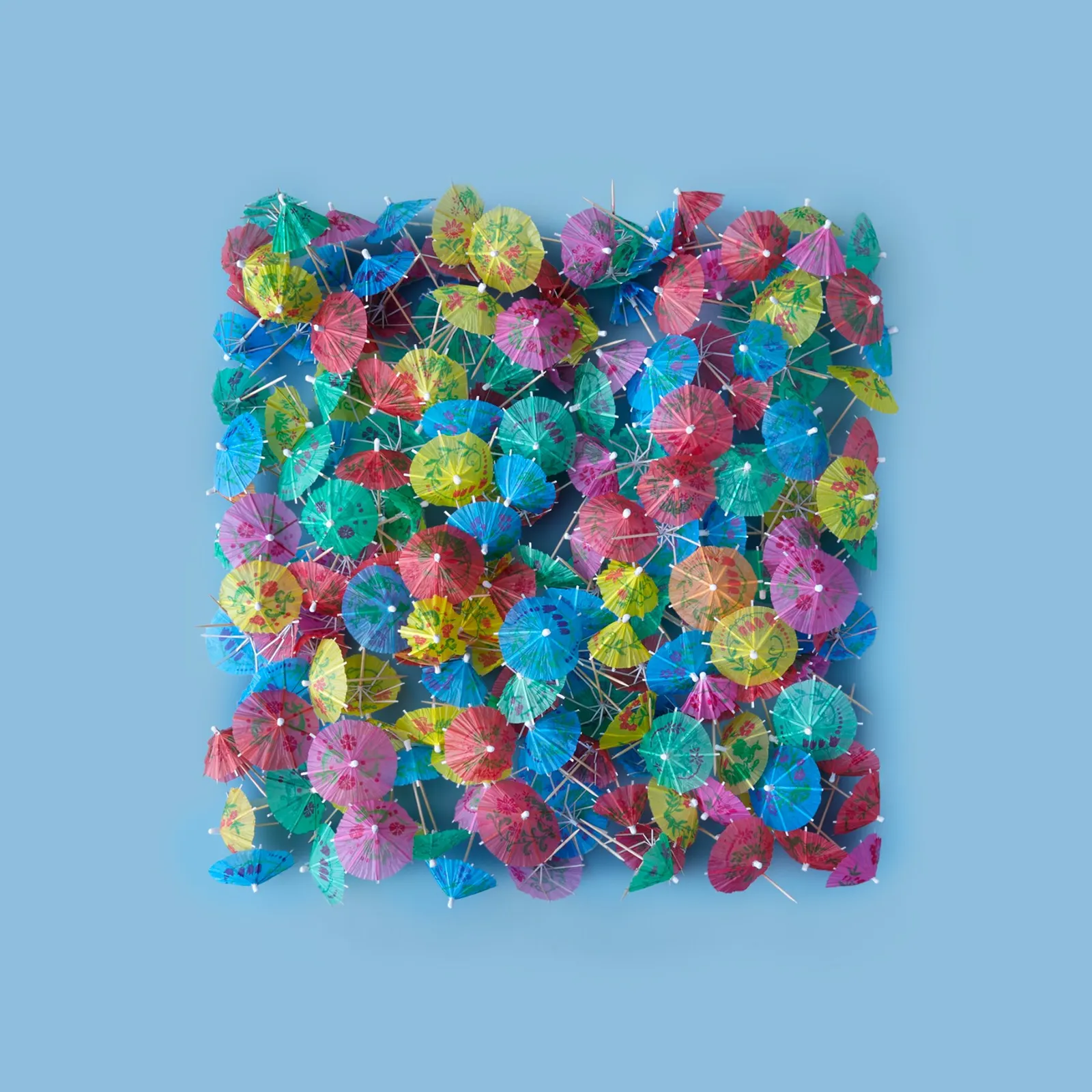 colorful paper cocktail umbrellas piled in a square on a pale blue background